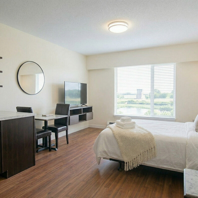 Bedroom detail with made bed, round mirror, desk, and window with a view